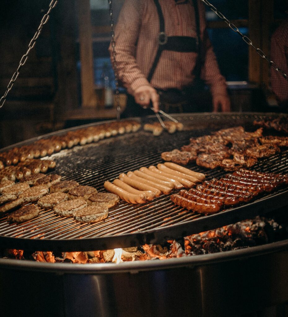 Delicious assortment of German sausages and meats grilling over open flame. Authentic street food vibe.